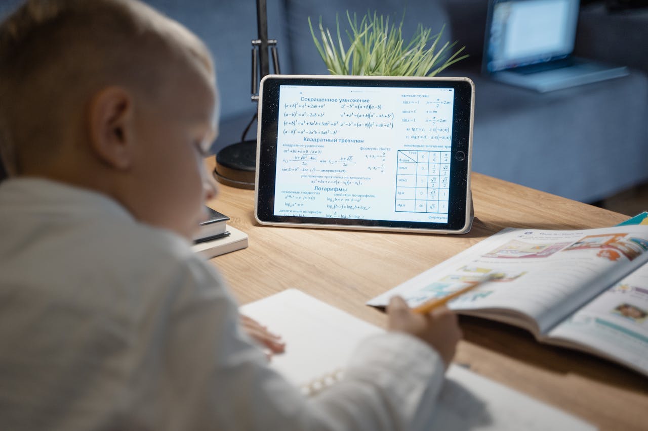 A young boy focuses on math problems on a tablet while studying at a desk indoors.