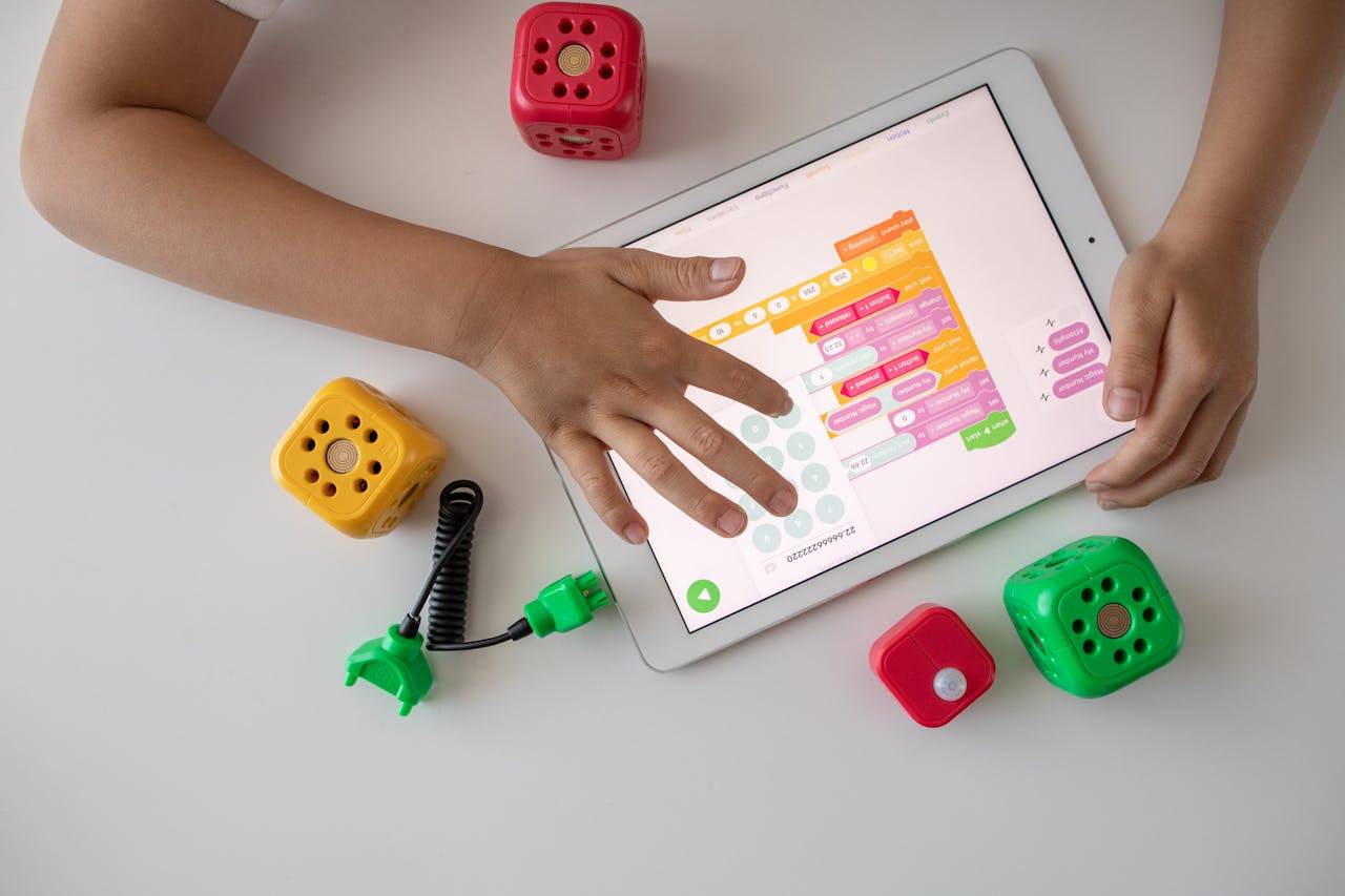 Child using digital tablet for coding education alongside colorful toy blocks.