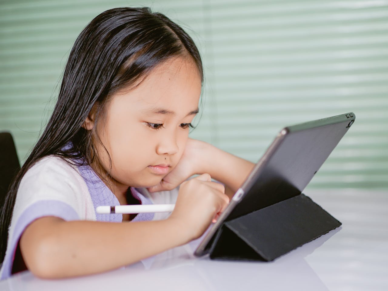 A young girl using a tablet for online learning, focused and engaged with her digital pen.